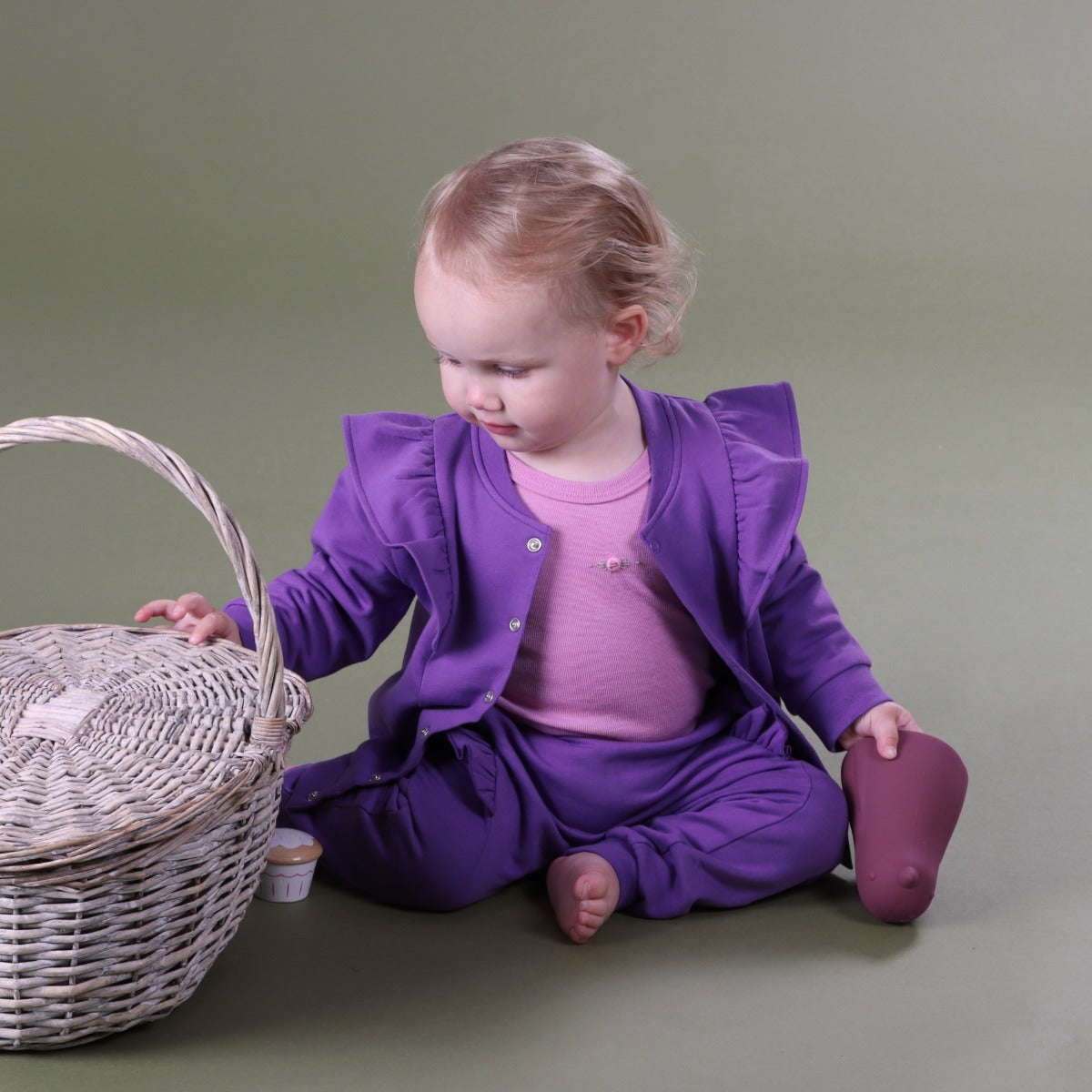 Baby girl sitting with a basket wearing Cotton Fleece Frill Jacket pairing it with pant and merino top:swatch_image