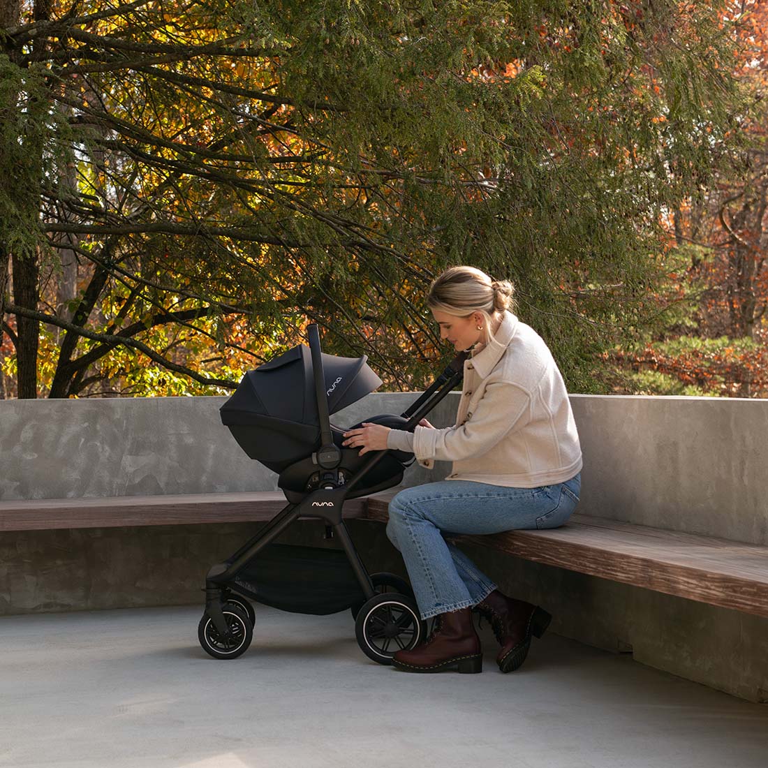 Mother sitting with Nuna Triv Next Caviar pram side view attached with Pipa capsule