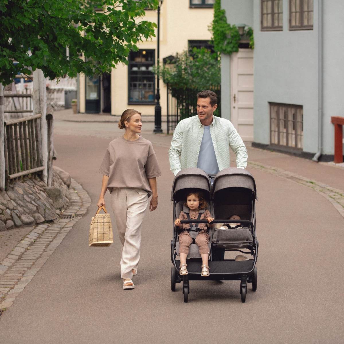 Couple walking with Trvl Dbl stroller with one kid sitting and another sleeping