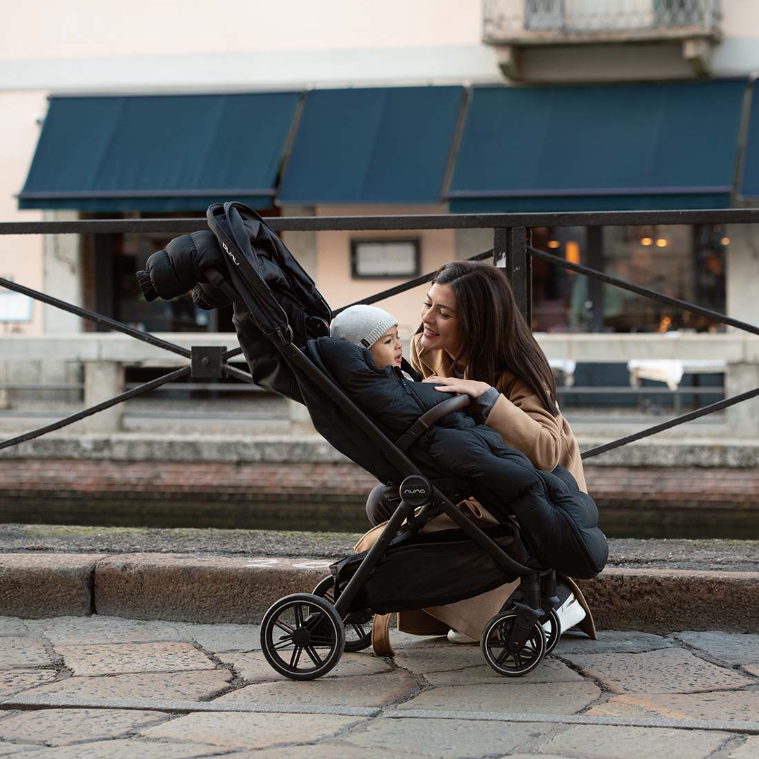 Mother on road with kid in a stroller with Nuna winter set footmuff
