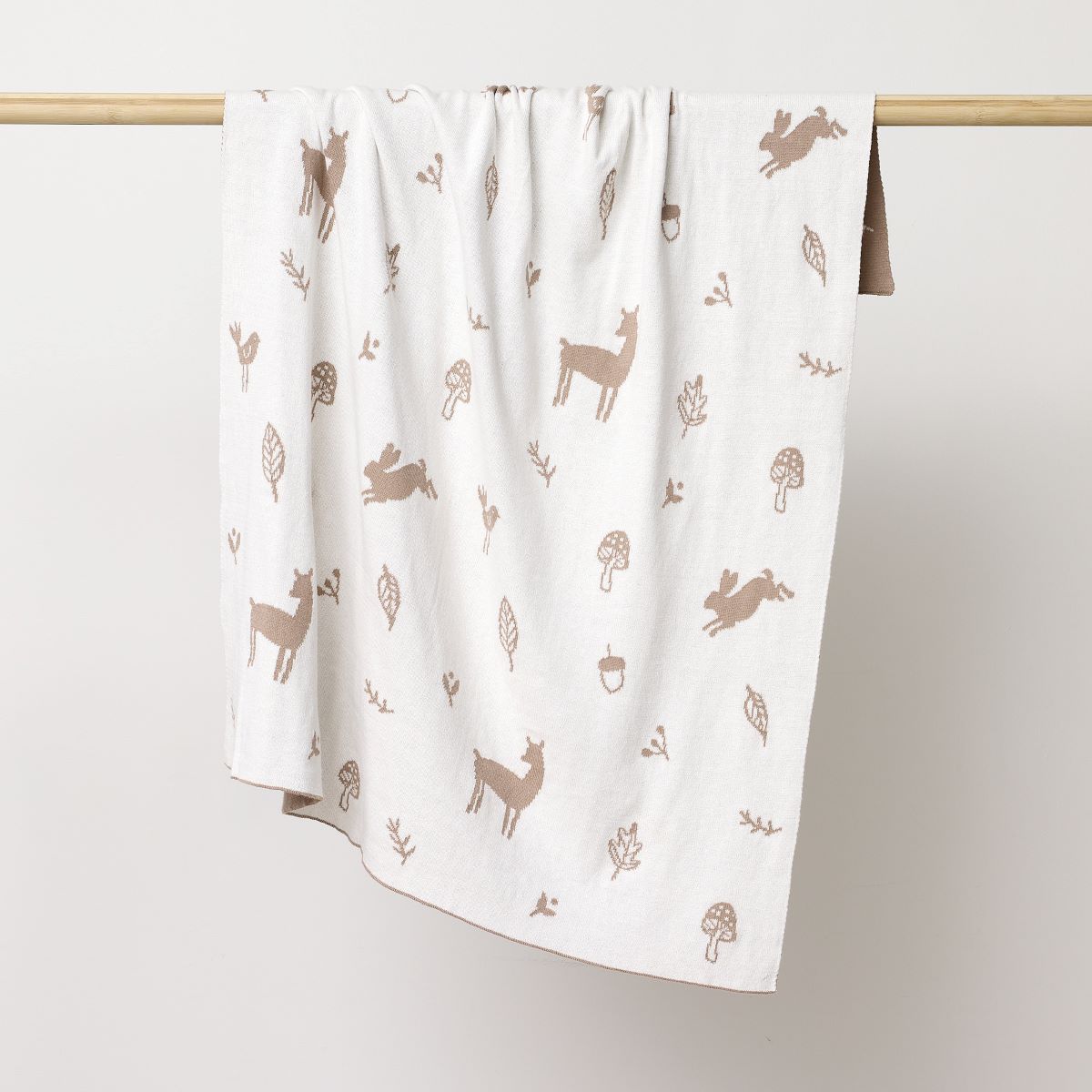 Reversed white coloured blanket with sparrows, deers, flowers and leavers printed in mushroom hanging on the wooden rod to display.