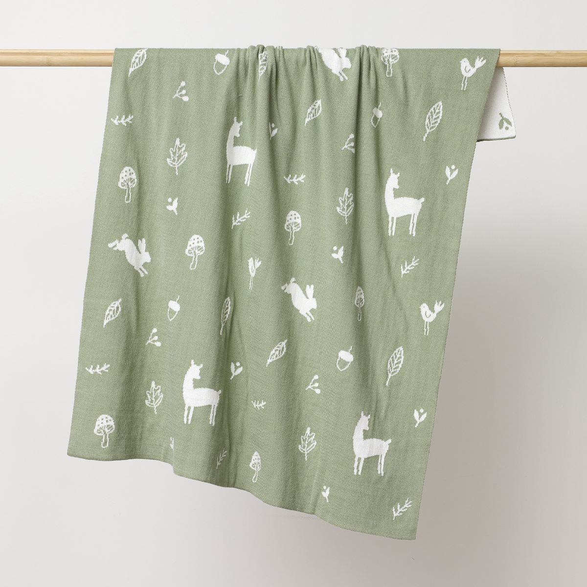 Thyme coloured blanket with deer's, bunnies, flowers and leavers printed in white hanging on the wooden rod to display.:image,small_image,thumbnail,swatch_image