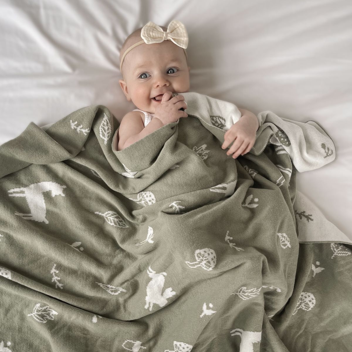 Happy Baby sleeping with thyme coloured blanket with deer's, bunnies, flowers and leavers printed in white.