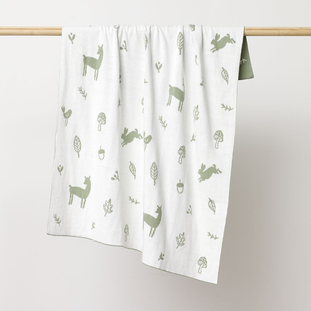 Reversed white coloured blanket with deer's, bunnies, flowers and leavers printed in thyme hanging on the wooden rod to display.